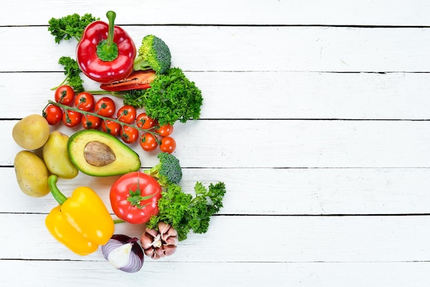 Fresh vegetables on a white wooden background Avocados tomatoes garlic parsley paprika Top view Free space for your text