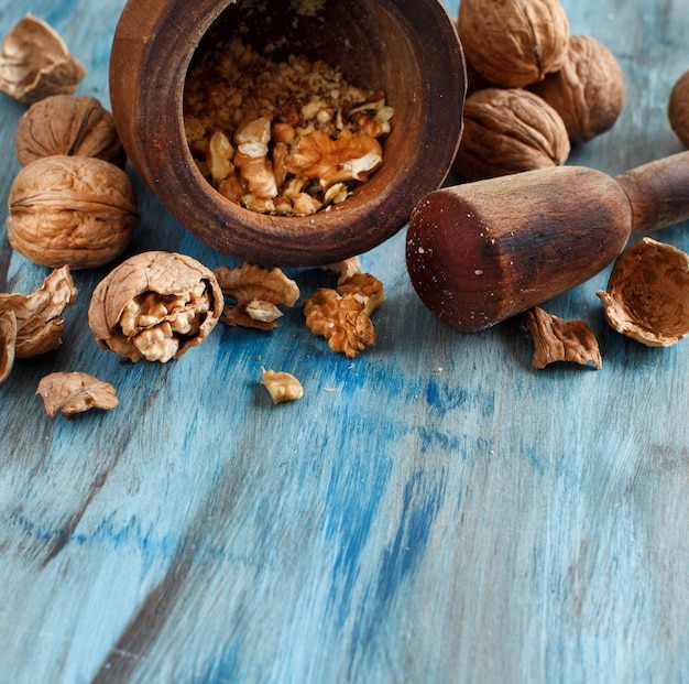 Fresh walnuts with mortar and pestle on a blue wooden table close up