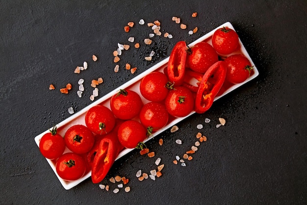 Fresh washed cherry tomatoes and paprika slices on a white oblong dish with pink salt and water drops on a black