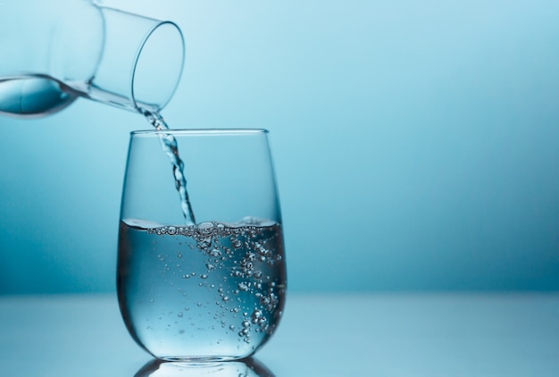 Fresh water pouring from the jug into a glass on the blue background. Drink water is important for optimal health