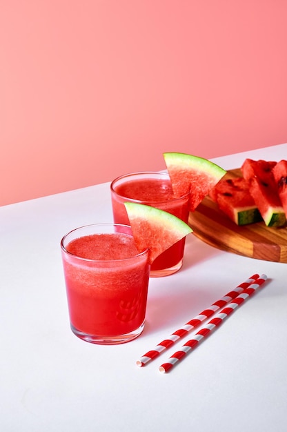 Fresh watermelon juice or smoothie in glasses with watermelon pieces on pink background