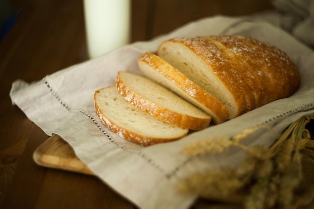 Fresh white bread on the linen textile and wooden table with milk glass and grains. Food photography -Bakery concept. slice homemade white wheat bread and kitchen towel. loaf of bread on linen napkin