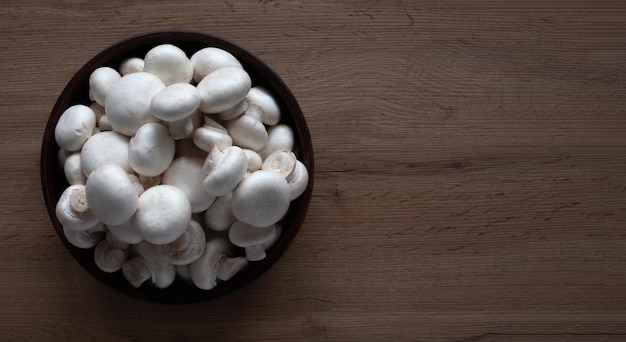 Fresh white mushrooms in a bowl on a wooden table top view