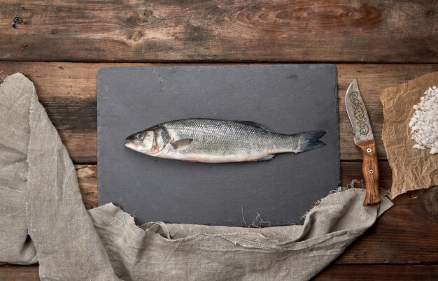 Photo fresh whole sea bass fish on black board