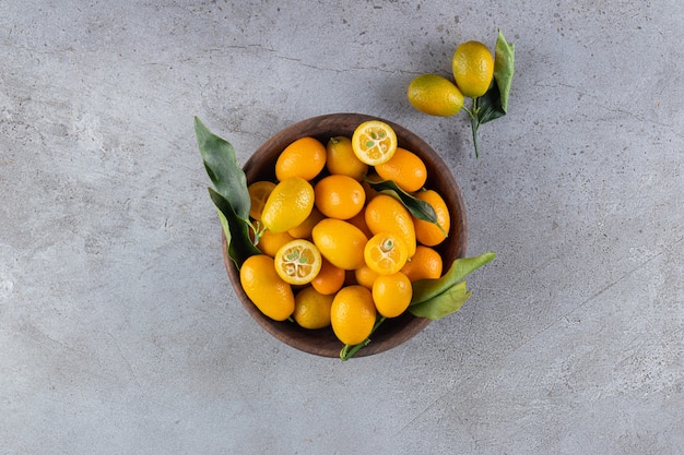 Fresh whole and sliced citrus cumquat fruits with leaves placed in wooden bowl