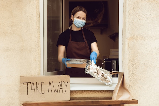 Fresh. Woman preparing drinks and meals, wearing protective face mask and gloves. Contactless delivery service during quarantine coronavirus pandemic. Take away concept. Recycable mugs, packages.