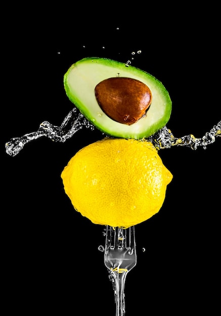 Fresh yellow lemon and avocado on a fork in splashes of water on a black background