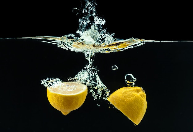 Fresh yellow lemon in water splash on black