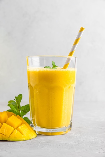 Fresh yellow mango smoothie in a glass with straw fresh fruits and mint Summer tropical drink