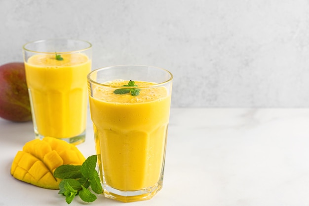 Fresh yellow mango smoothie in glasses with fresh fruits and mint Summer tropical drink on white background