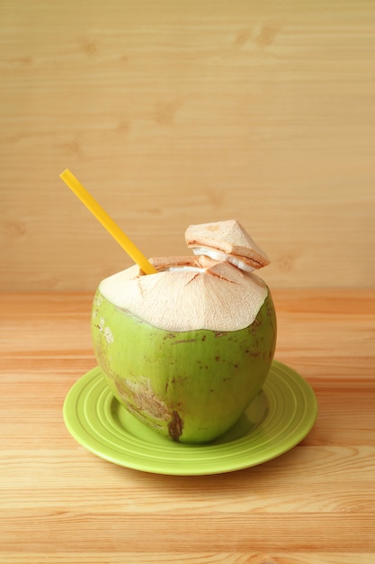 Fresh young coconut with yellow straw on a green plate ready for drinking