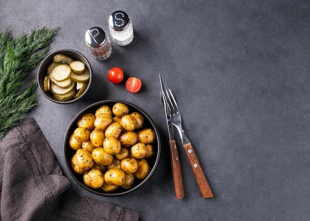 Fresh young roasted baby potatoes in a black pan with tomatoes and herbs on a dark background