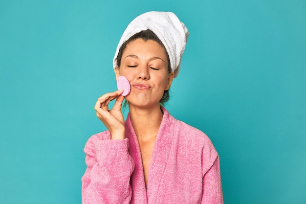 Freshfaced woman with makeup sponge smiling in pink robe