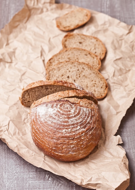 Freshly baked bread loaf with pieces on white wooden board