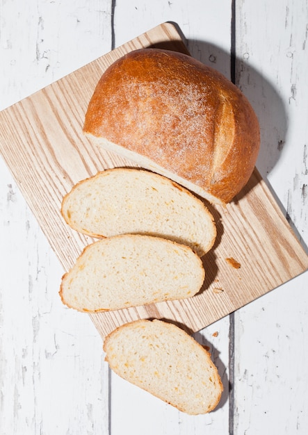 Freshly baked bread loaf with pieces on wood boardon white wooden board