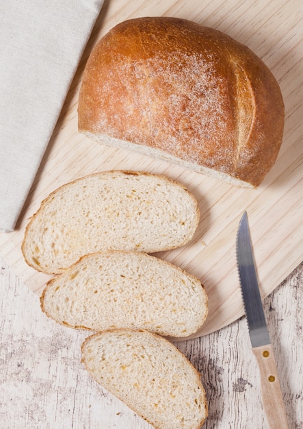 Freshly baked bread loaf with pieces on wood boardon wooden board with kitchen towel and knife