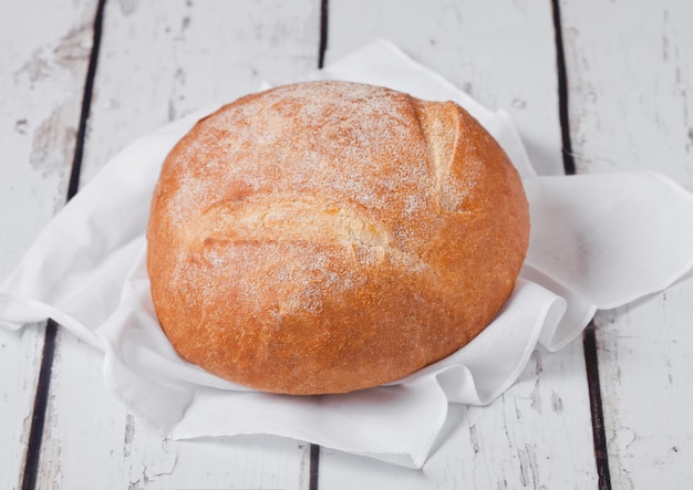 Freshly baked  bread with  kitchen towel and wheat on white wooden board