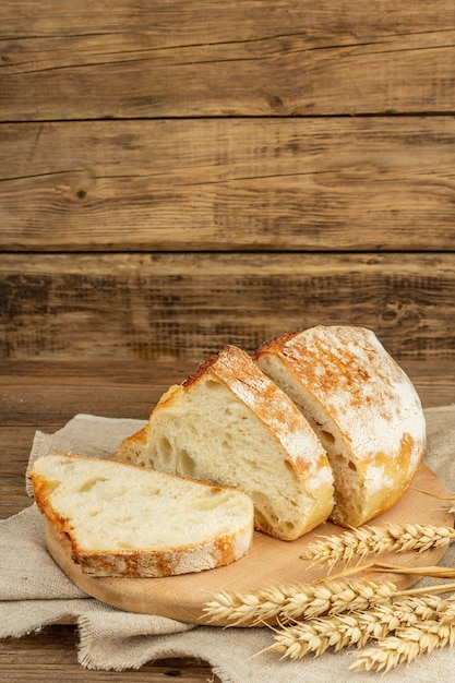 Freshly baked bread with wheat ears, fragrant pieces on a cutting board. Vintage wooden boards table, ready baked goods, copy space