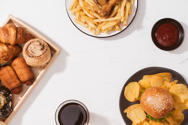 Freshly baked buns, big hamburger, fried crispy chicken and french fries on white table - Unhealthy food concept