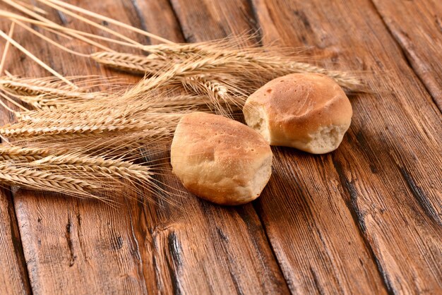 Freshly baked buns and ears of wheat on a wooden table