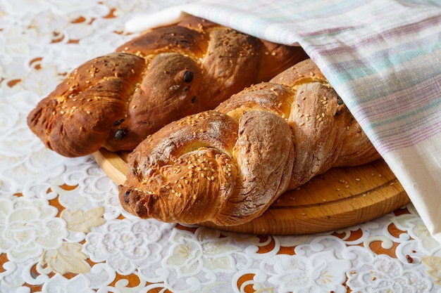 Freshly baked challah with sesame seeds for Shabbat on a wooden board on a white tablecloth