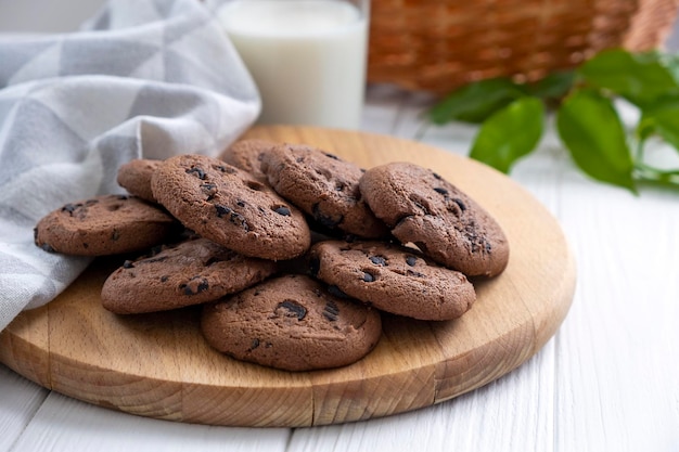 Freshly baked chocolate chip cookies on wooden board with glass of milk and kitchen towel Recipe of shortbread cookies with chocolate chips Snack or treat for tea or coffee