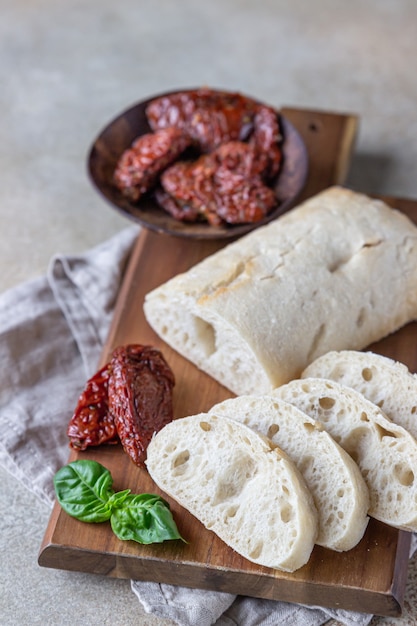 Freshly baked ciabatta bread on wooden plate with sun-dried tomatoes and basil.