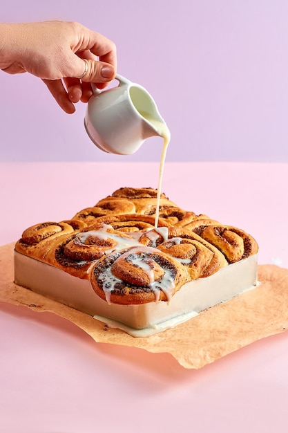 Freshly baked cinnamon rolls topped with creamy sweet cheese on a pink background