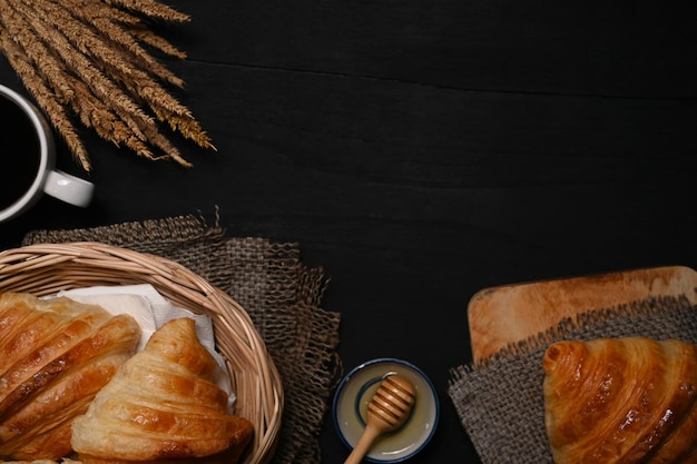 Freshly baked homemade butter croissant in wicker basket decorated with wheat on black wooden table