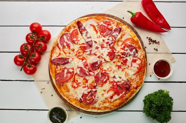 Freshly baked pizza with smoked sausages red pepper and tomatoes served on wooden background with sauce and herbs Food delivery concept Restaurant menu