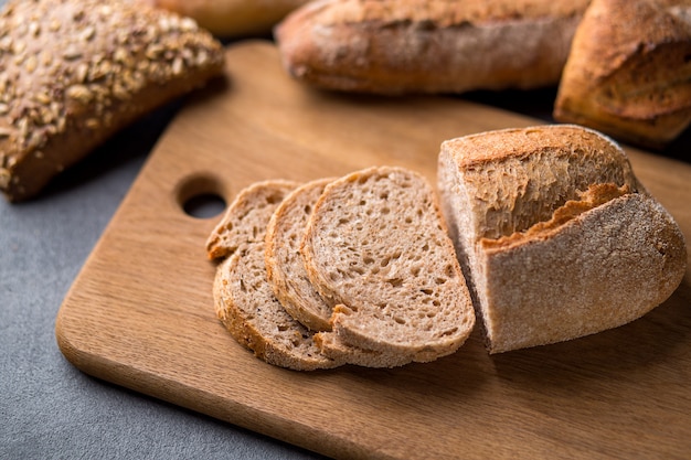 Freshly baked sliced bread on wooden cutting board on the grey stone table