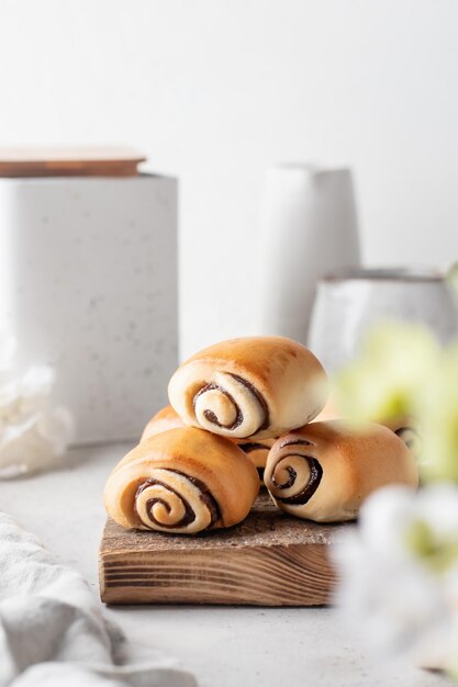 Freshly Baked Sweet Cinnamon Rolls for breakfast on wooden board in composition on white kithen table Easter traditional pastry food