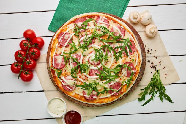 Freshly baked tasty pepperoni pizza with salami mozzarella cheese and rukkola served on wooden background with tomatoes sauce and herbs Food delivery concept Restaurant menu