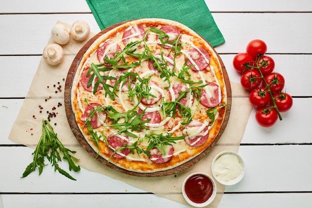 Freshly baked tasty pepperoni pizza with salami mozzarella cheese and rukkola served on wooden background with tomatoes sauce and herbs Food delivery concept Restaurant menu