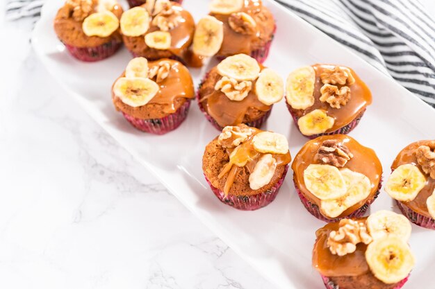 Freshly bakes banana nut bread muffins drizzled with homemade caramel, decorated with walnuts and banana chips.