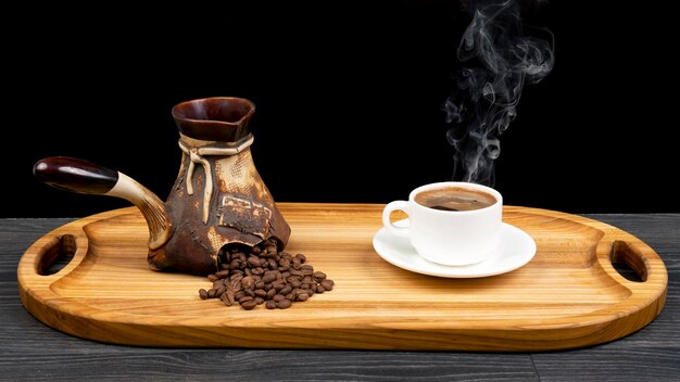 Freshly brewed hot black coffee in a white cup on a wooden board next to a ceramic turkey with coffee beans.