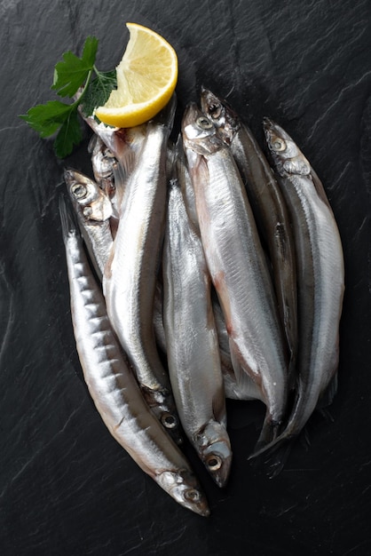 Freshly caught small marine fish on a plate on a gray concrete background with copy space Capelin ready to cook with lemon coarse sea salt Top view flat