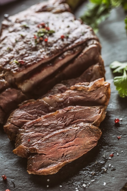 Freshly grilled beef steak on slate plate with salt pepper rosemary and parsley herbs. Sliced pieces of juicy beef steak.