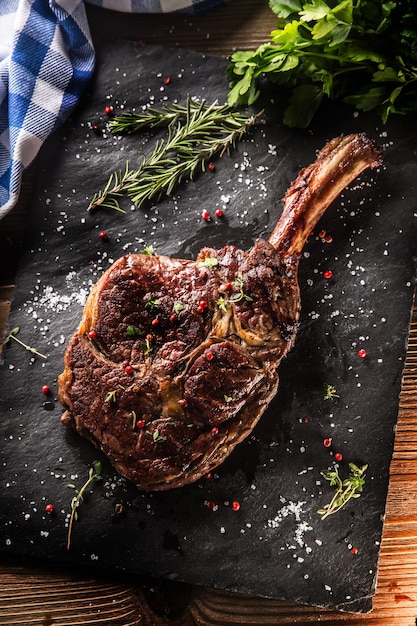 Freshly grilled tomahawk steak on slate plate with salt pepper rosemary and parsley herbs