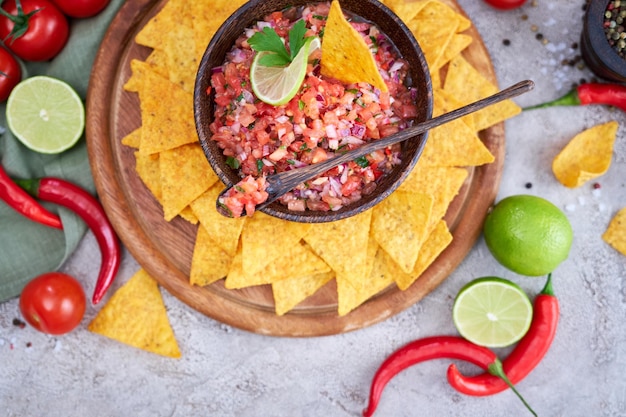 Freshly made salsa dip sauce with nacho chips on wooden board