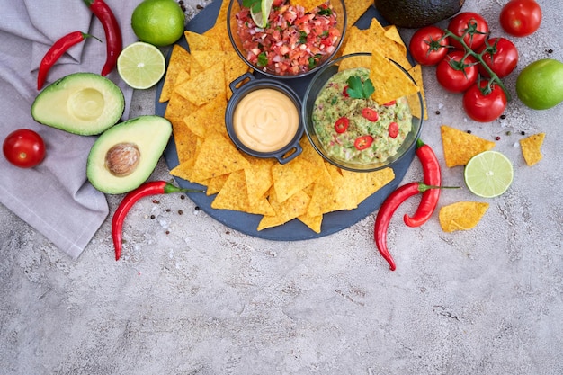 Freshly made salsa and guacamole dip sauce with nacho chips on stone serving board