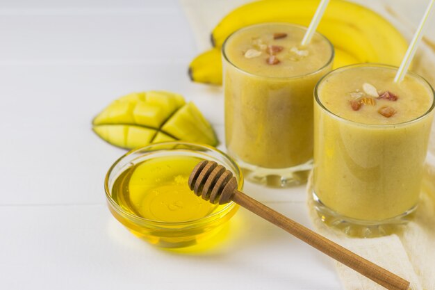 Freshly made smoothies with mango, banana, orange, honey and cereal on a wooden table