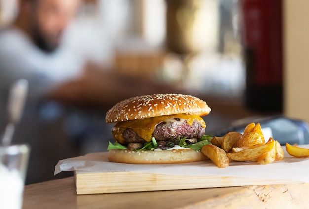 Freshly prepared burger with melted cheese on wooden board.