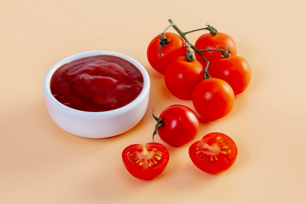 Freshly prepared ketchup with ripe red tomatoes on orange background