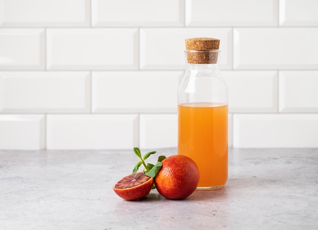 Freshly squeezed orange juice in a bottle on the kitchen table with fresh red oranges The concept of a healthy drink Front view and copy xAspace