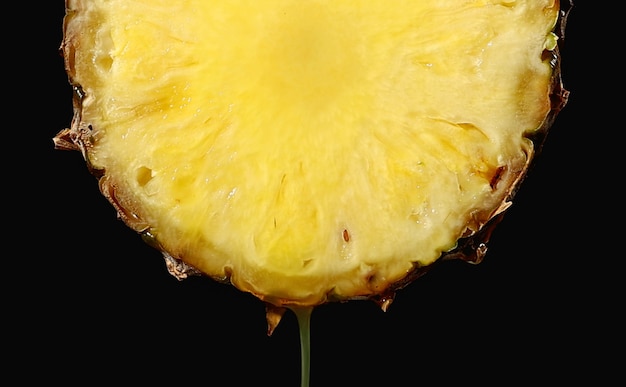 Freshly squeezed pineapple juice flows from the ripe fruit slice close - up on a black background