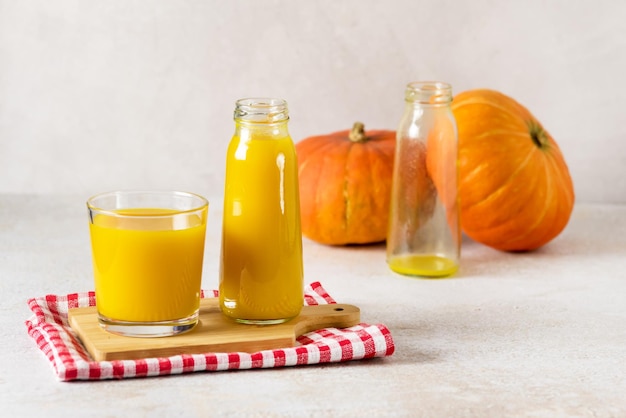 Freshly Squeezed Pumpkin Juice in Glass Bottle with Yellow Juice on Wooden Tray Napkin