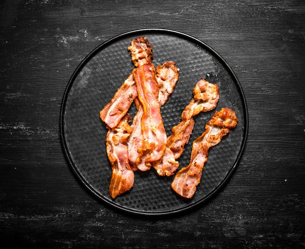 Fried bacon on a plate. On a black wooden background.