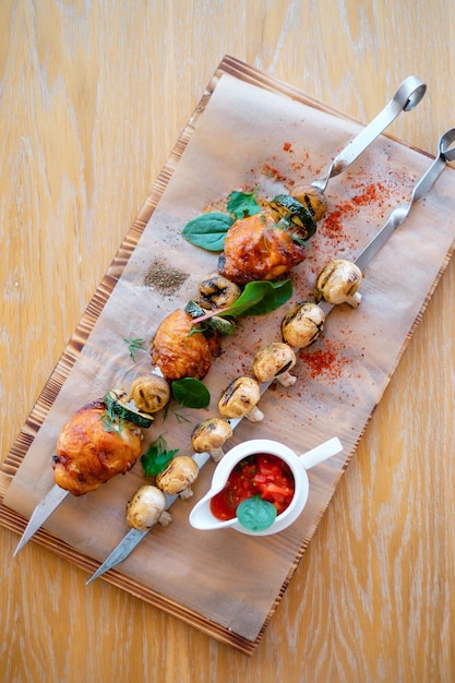 Photo fried barbeque chicken on a skewer with potatoes and vegetables grilled bbq decorated with vegetables and sauce on wooden table and parchment paper