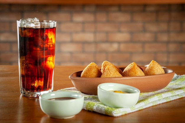 Fried brazilian croquettes coxinha de frango with iced soda in a kitchen with bricks wall